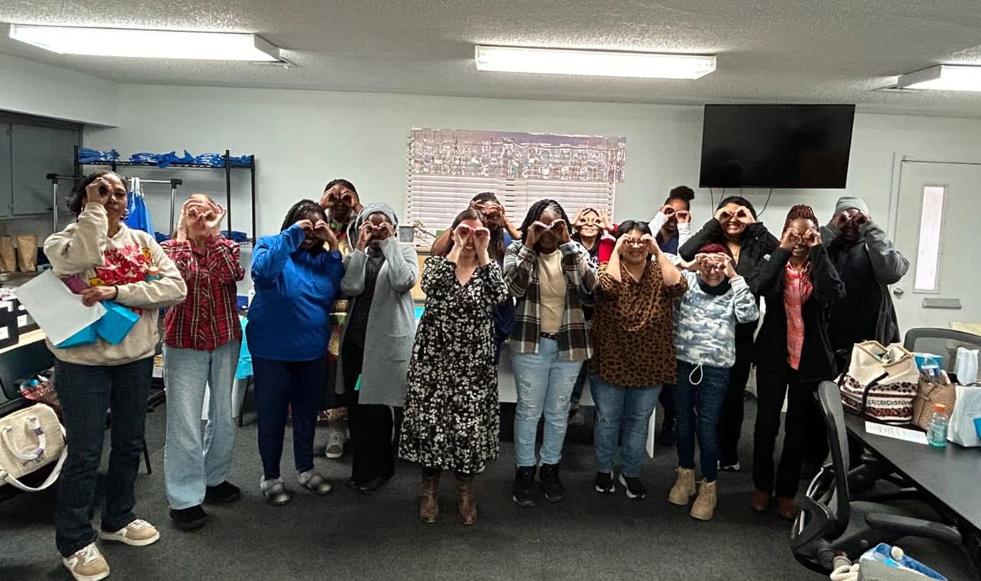 A large group of care staff making binocular gestures around their eyes during a training session